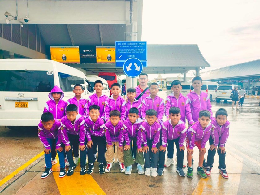 Baysavanh FC under-10 players in purple tracksuits pose with an official before travelling to Chiang Mai